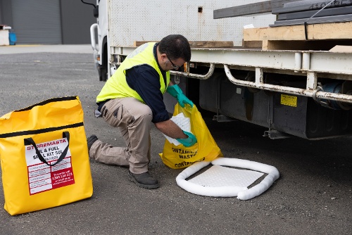 staff cleaning up soiled spill kit absorbents after containing a vehicle oil leak